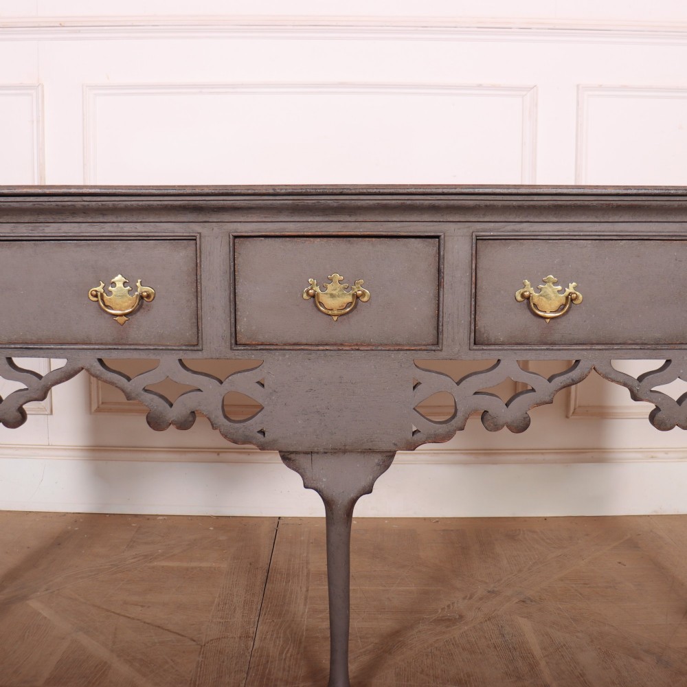 A grey-painted antique dresser base featuring three drawers with brass handles, a decorative pierced fretwork apron, and cabriole legs. View III