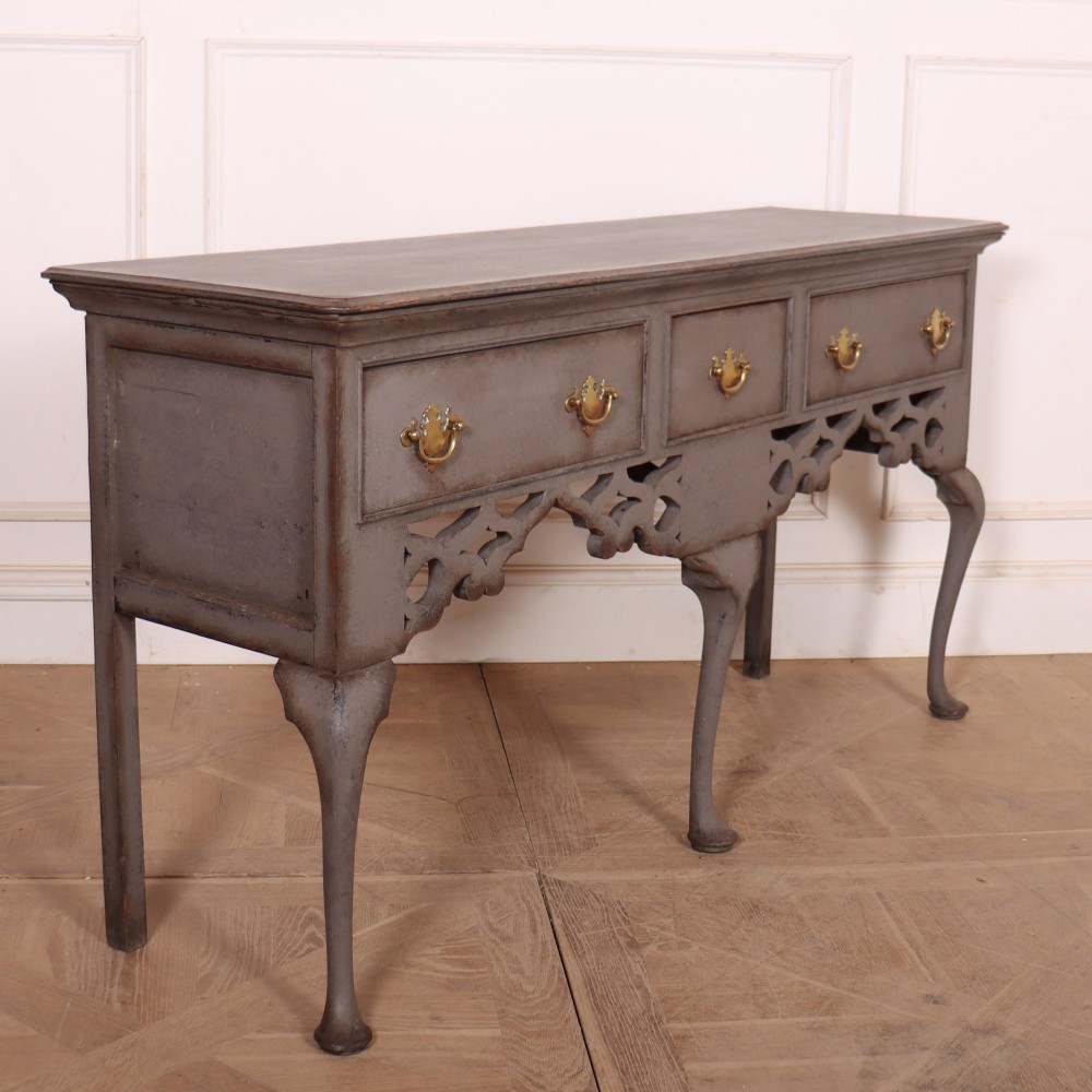 A grey-painted antique dresser base featuring three drawers with brass handles, a decorative pierced fretwork apron, and cabriole legs. View VI