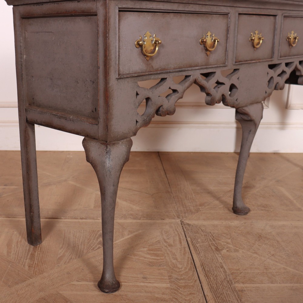 A grey-painted antique dresser base featuring three drawers with brass handles, a decorative pierced fretwork apron, and cabriole legs. View VII