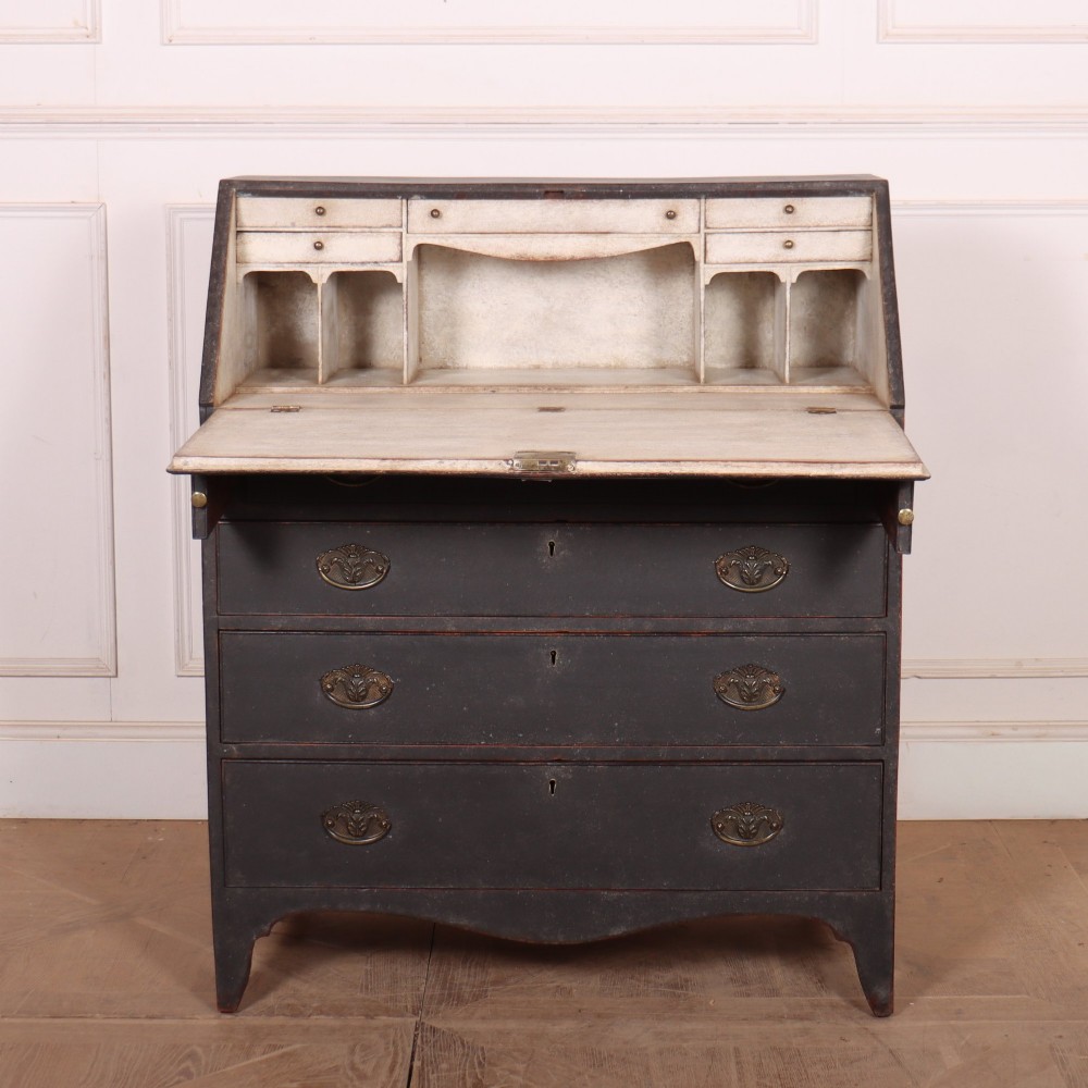 A small painted English bureau secretaire featuring a dark grey exterior, three lower drawers with brass handles, and a drop-front slant lid opening to a cream fitted interior with pigeonholes.