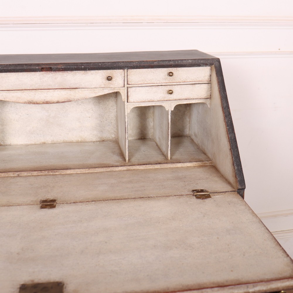 A small painted English bureau secretaire featuring a dark grey exterior, three lower drawers with brass handles, and a drop-front slant lid opening to a cream fitted interior with pigeonholes. View V