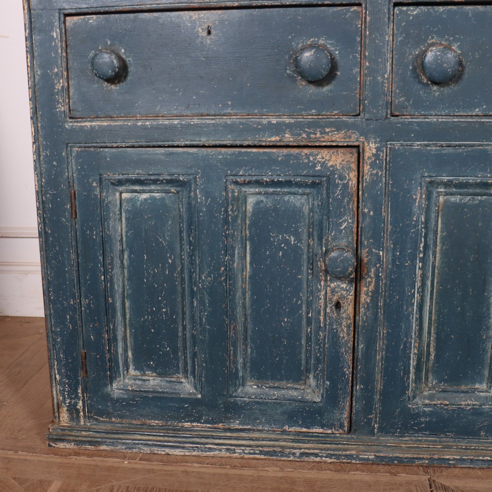 A large two-part dark blue painted timber dresser featuring a glazed upper display section with grid-paned doors and a dentil corniced top, resting on a base with three drawers and three panelled cupboard doors. View III