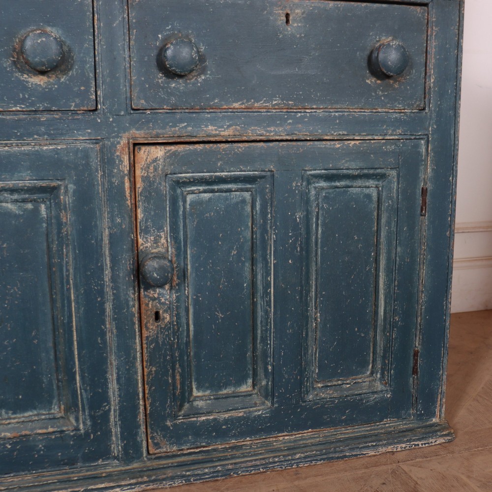 A large two-part dark blue painted timber dresser featuring a glazed upper display section with grid-paned doors and a dentil corniced top, resting on a base with three drawers and three panelled cupboard doors. View VII
