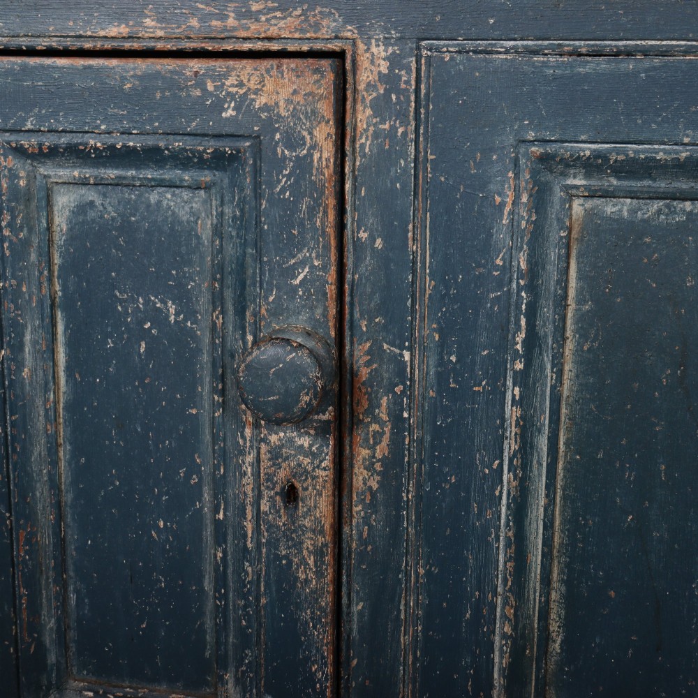 A large two-part dark blue painted timber dresser featuring a glazed upper display section with grid-paned doors and a dentil corniced top, resting on a base with three drawers and three panelled cupboard doors. View VIII