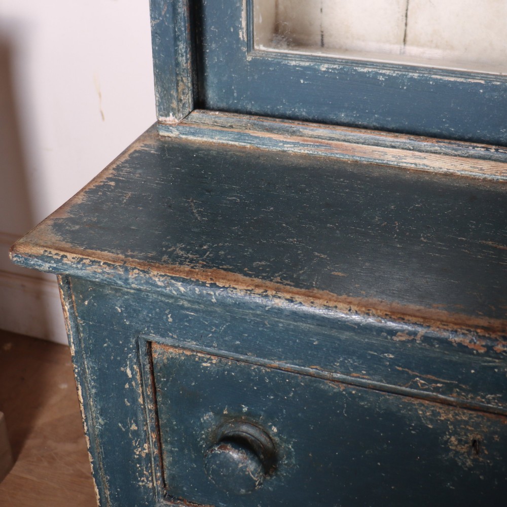 A large two-part dark blue painted timber dresser featuring a glazed upper display section with grid-paned doors and a dentil corniced top, resting on a base with three drawers and three panelled cupboard doors. View XII