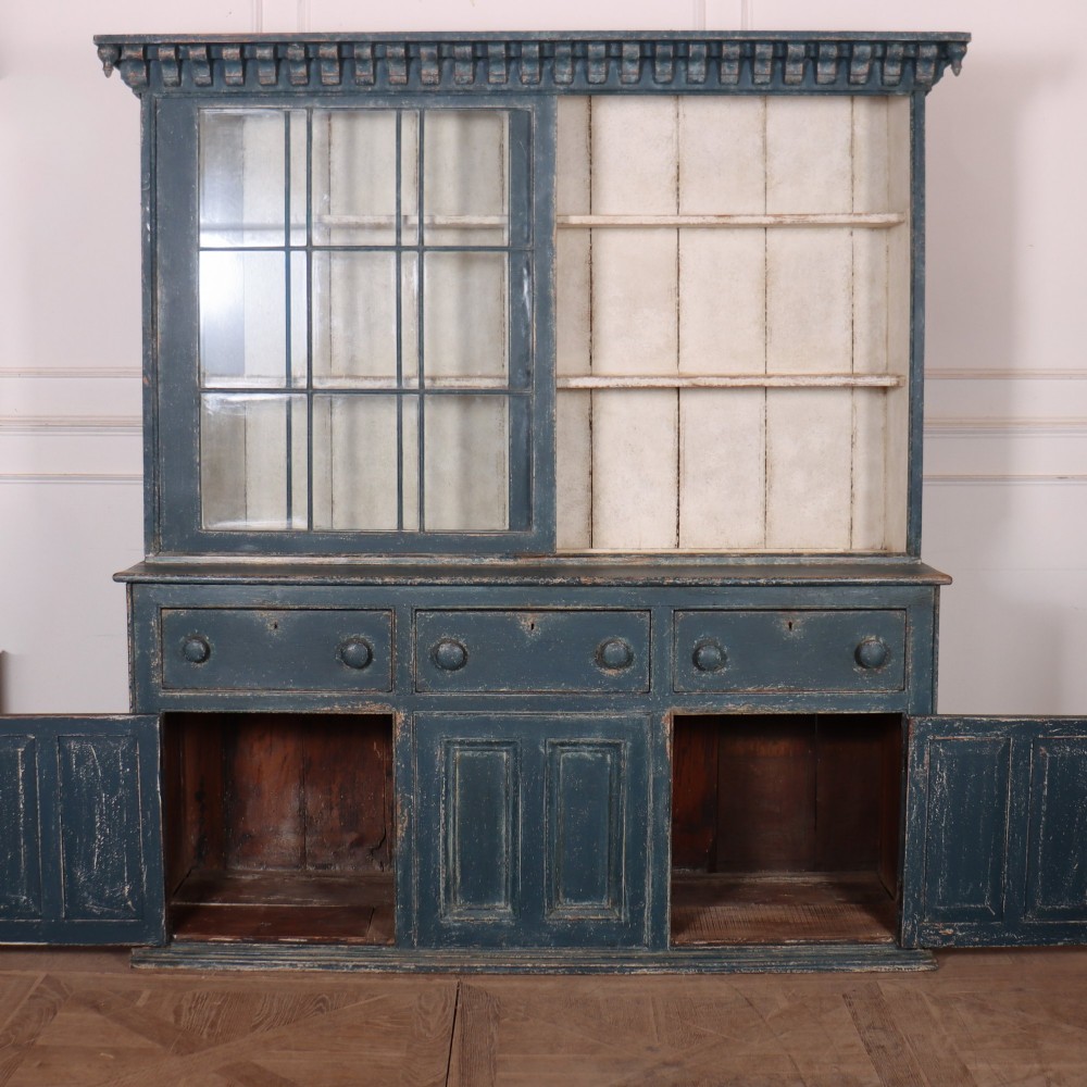 A large two-part dark blue painted timber dresser featuring a glazed upper display section with grid-paned doors and a dentil corniced top, resting on a base with three drawers and three panelled cupboard doors. View XIV