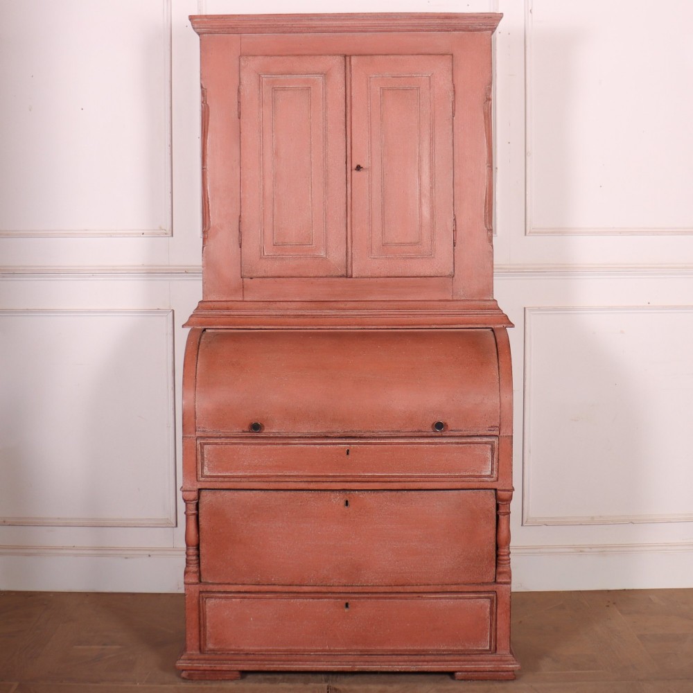 A two-piece Danish bureau bookcase featuring a terracotta red painted finish, upper panelled double cupboard doors, a cylinder roll-top desk centre, and three long drawers below.
