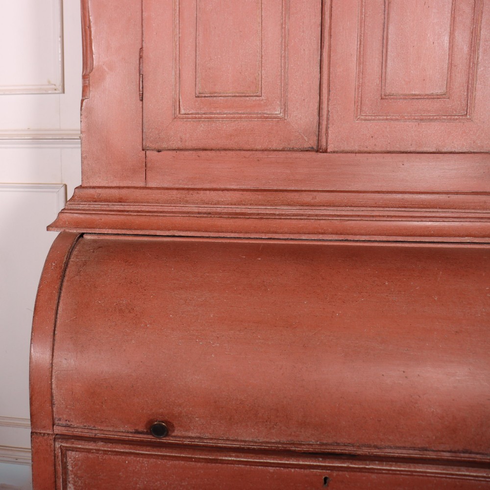 A two-piece Danish bureau bookcase featuring a terracotta red painted finish, upper panelled double cupboard doors, a cylinder roll-top desk centre, and three long drawers below. View V