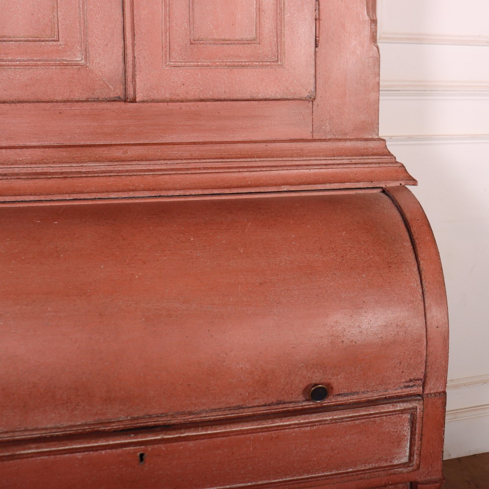 A two-piece Danish bureau bookcase featuring a terracotta red painted finish, upper panelled double cupboard doors, a cylinder roll-top desk centre, and three long drawers below. View VI