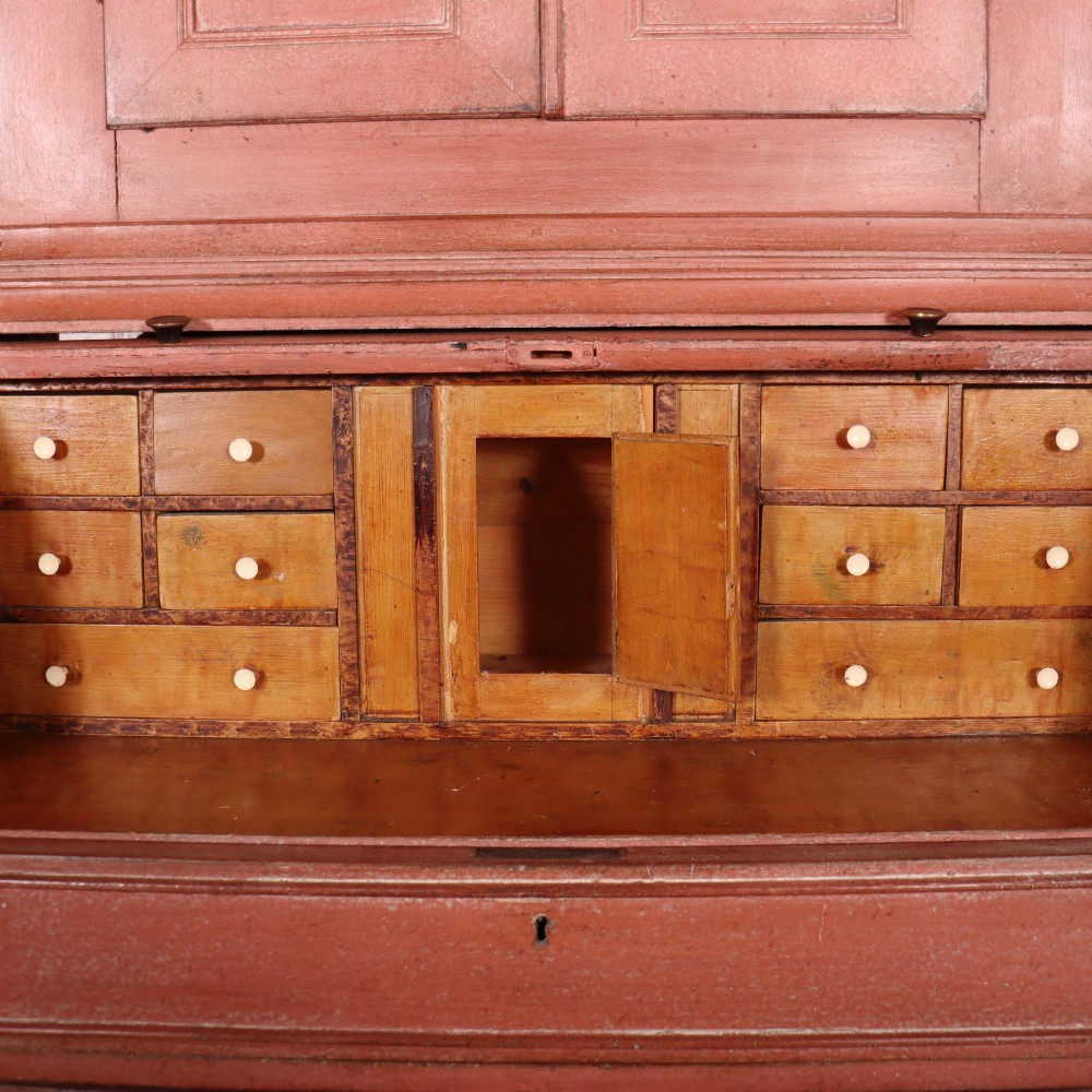 A two-piece Danish bureau bookcase featuring a terracotta red painted finish, upper panelled double cupboard doors, a cylinder roll-top desk centre, and three long drawers below. View X