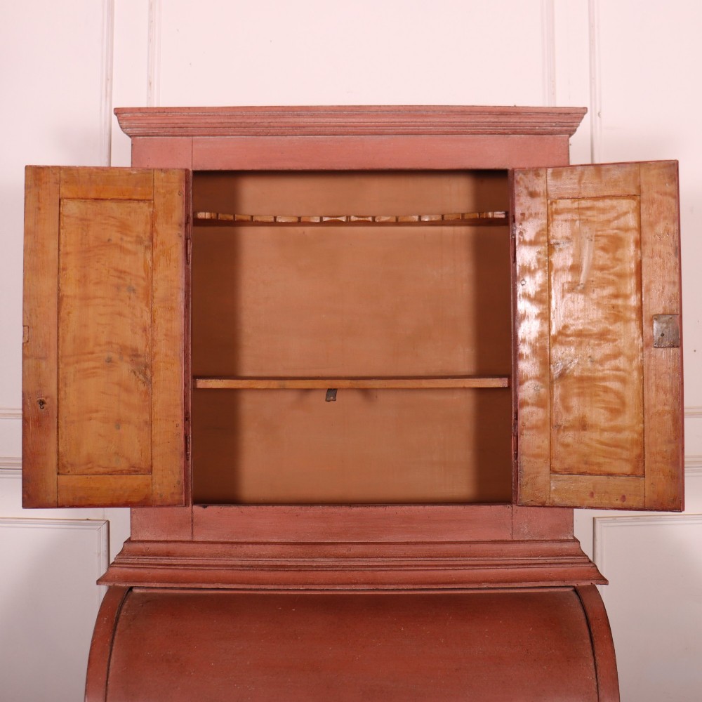 A two-piece Danish bureau bookcase featuring a terracotta red painted finish, upper panelled double cupboard doors, a cylinder roll-top desk centre, and three long drawers below. View XI