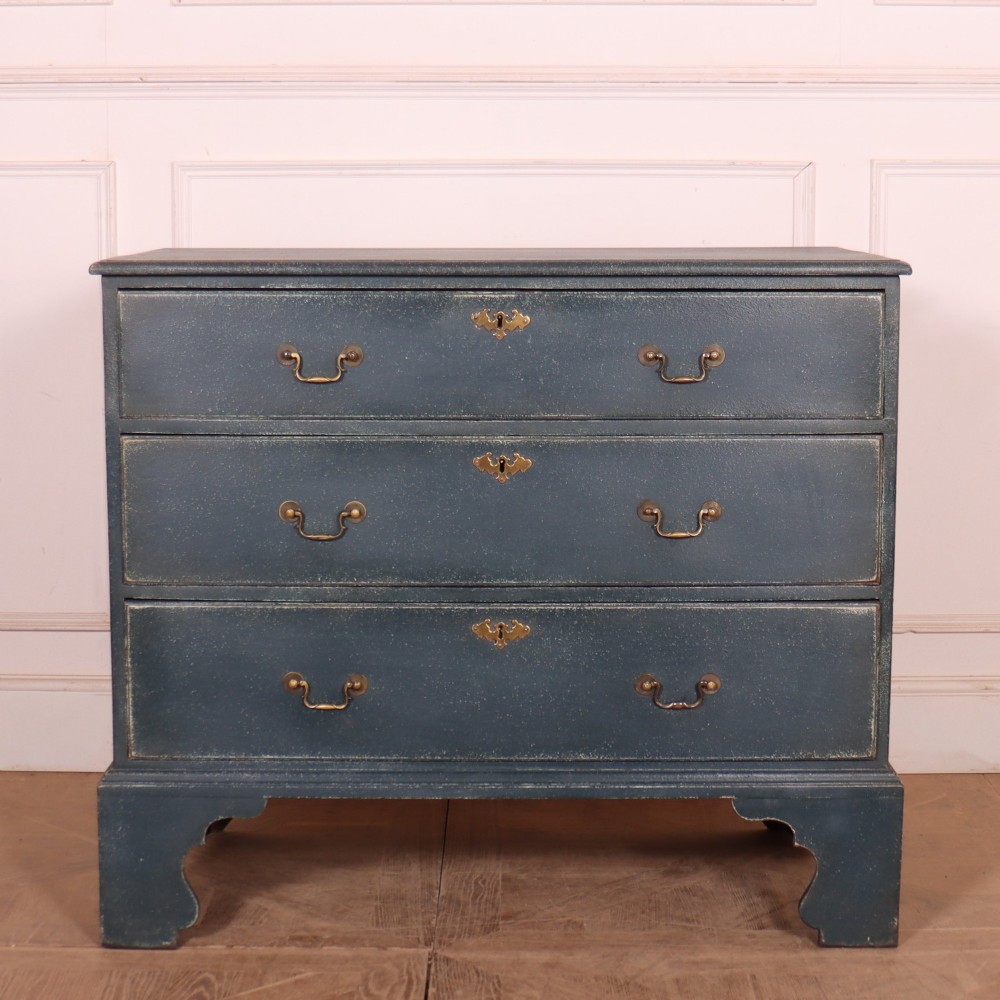 A three-drawer painted wooden chest featuring a dark blue painted finish, brass swan-neck handles, and shaped bracket feet.