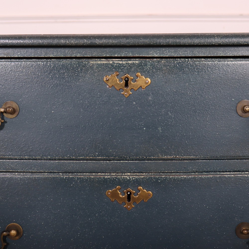 A three-drawer painted wooden chest featuring a dark blue painted finish, brass swan-neck handles, and shaped bracket feet. View VI