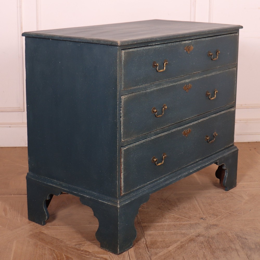 A three-drawer painted wooden chest featuring a dark blue painted finish, brass swan-neck handles, and shaped bracket feet. View VII
