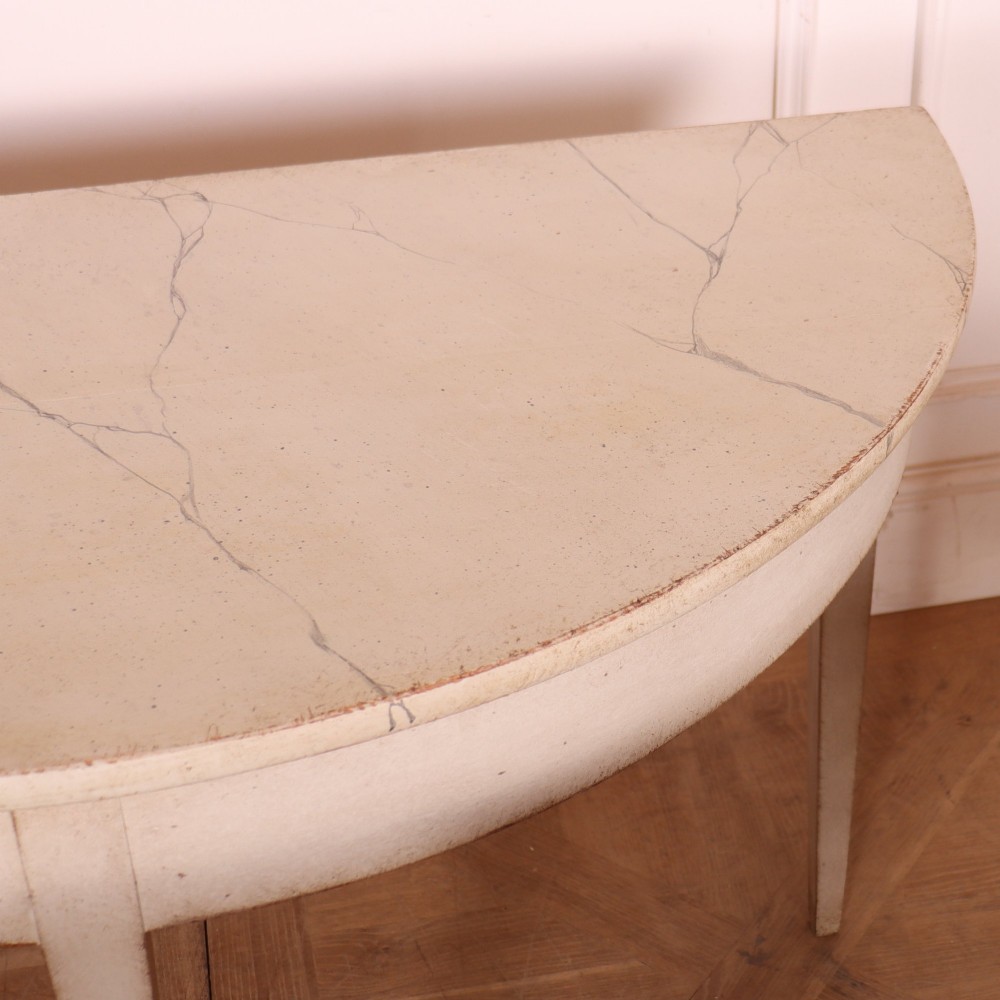 A pair of off-white painted semicircular demi lune console tables with slender tapered legs resting on a wooden parquet floor. View VII