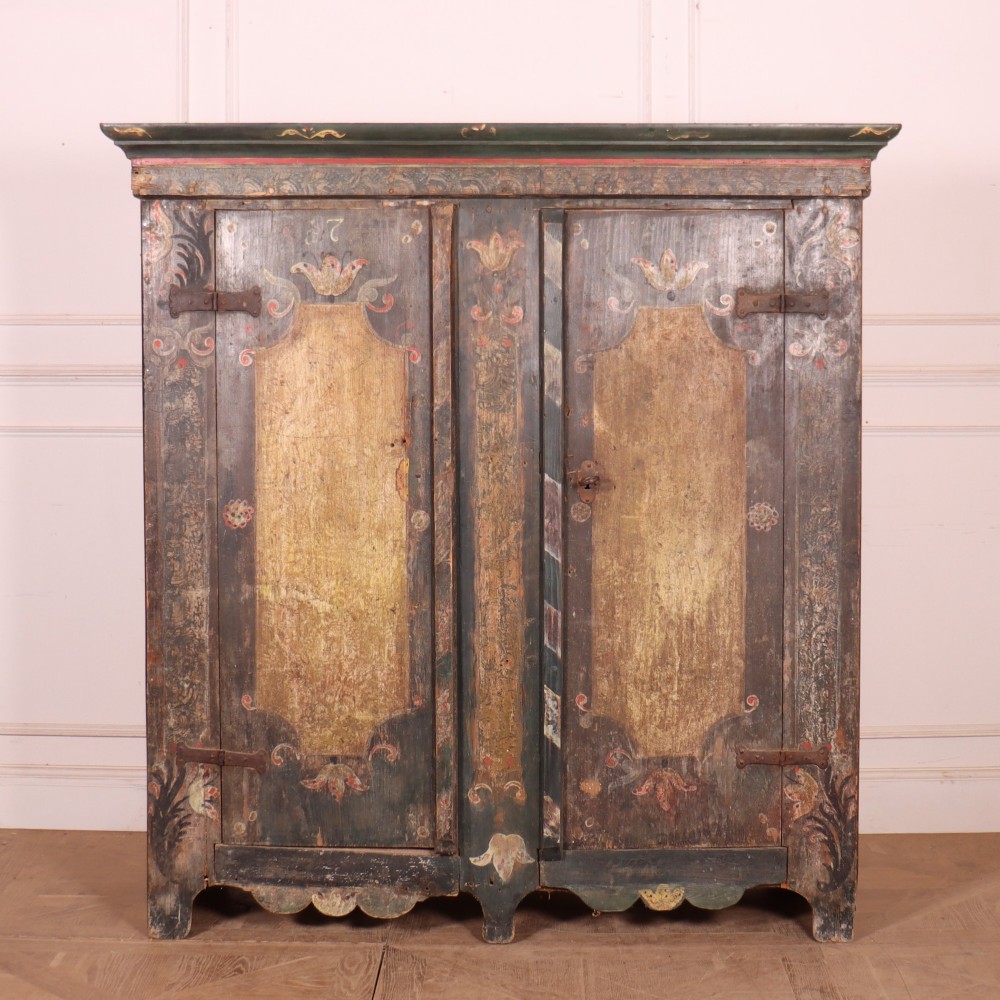 An antique two-door Austrian marriage cupboard featuring hand-painted floral motifs, central ochre panels, a scalloped base apron, and exposed iron strap hinges.
