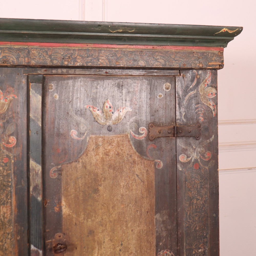 An antique two-door Austrian marriage cupboard featuring hand-painted floral motifs, central ochre panels, a scalloped base apron, and exposed iron strap hinges. View III