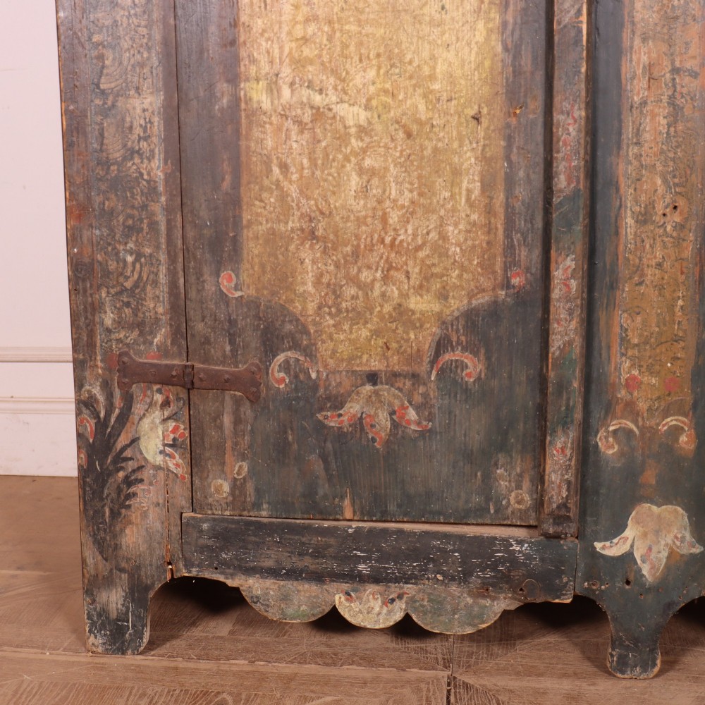 An antique two-door Austrian marriage cupboard featuring hand-painted floral motifs, central ochre panels, a scalloped base apron, and exposed iron strap hinges. View IV