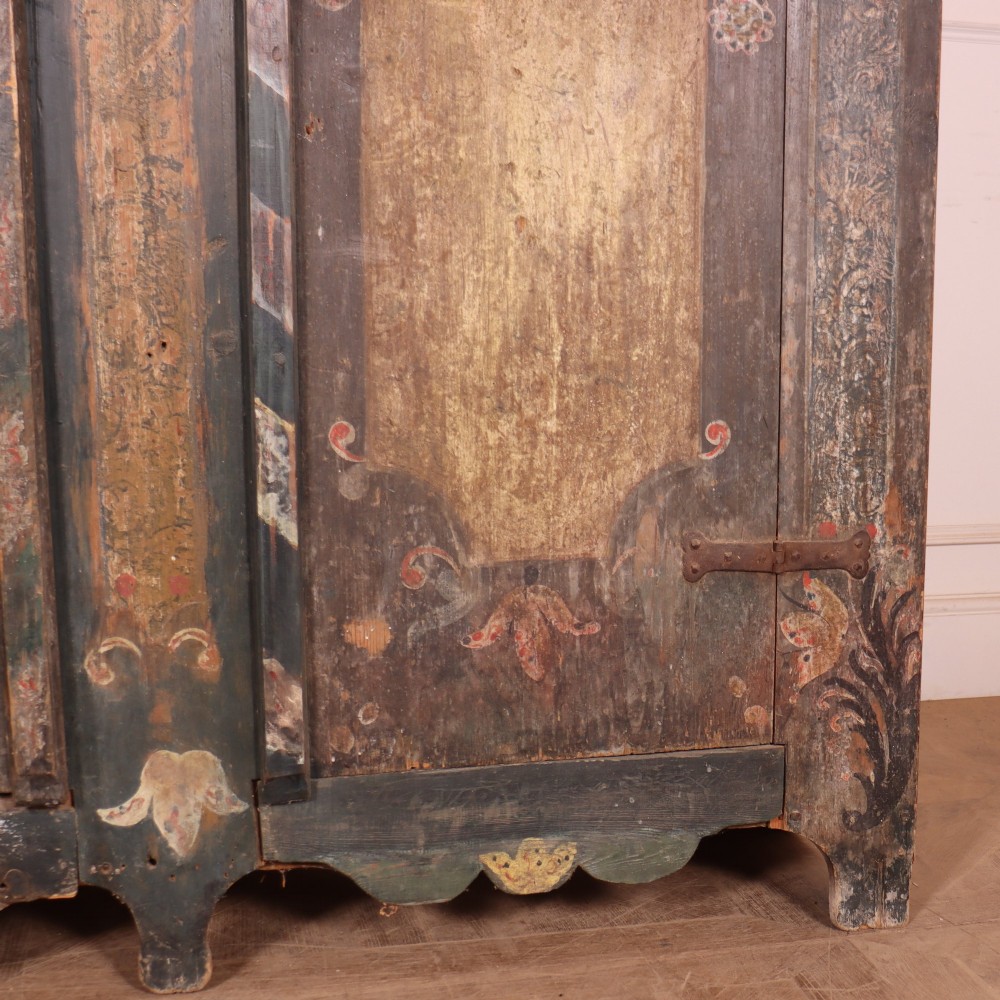An antique two-door Austrian marriage cupboard featuring hand-painted floral motifs, central ochre panels, a scalloped base apron, and exposed iron strap hinges. View V