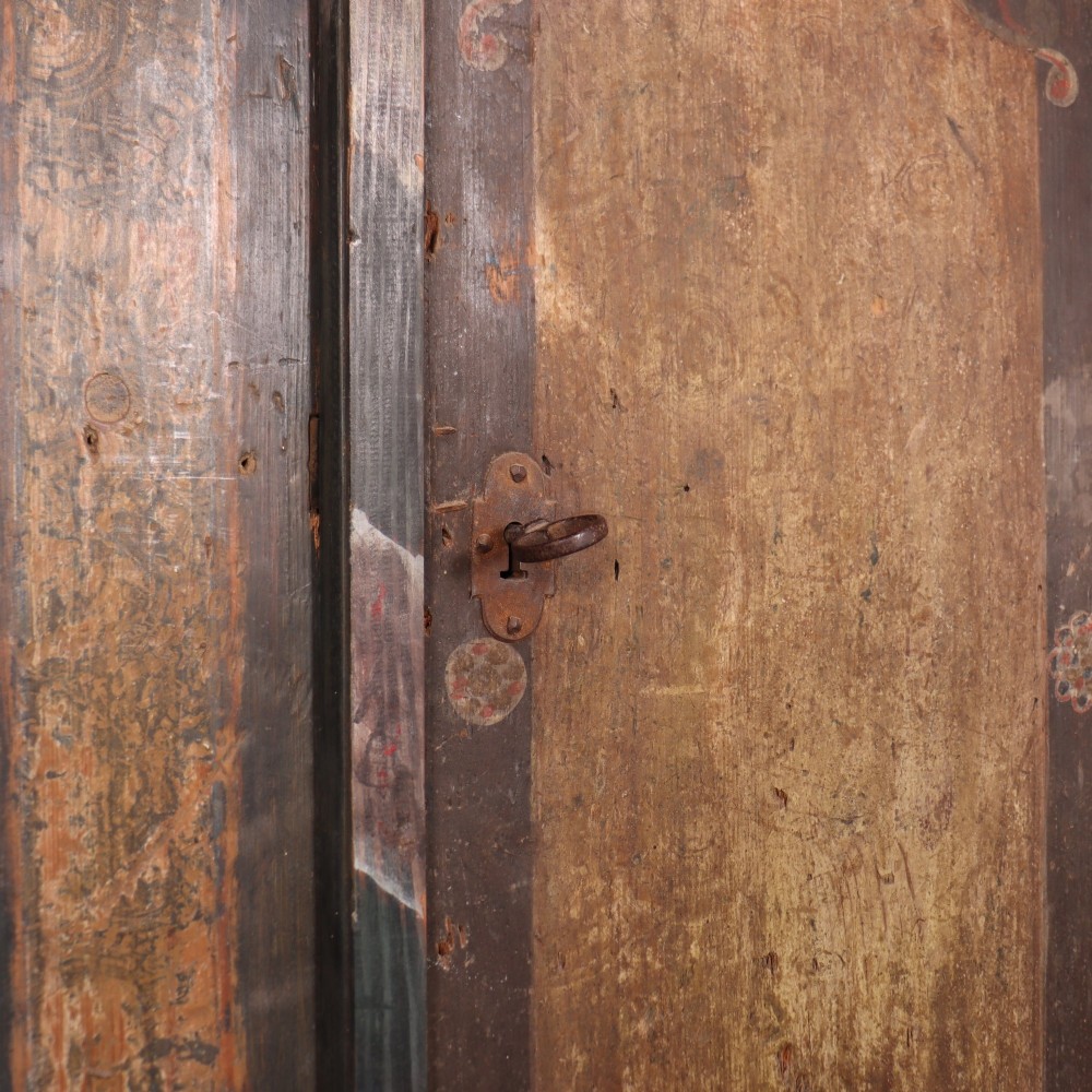 An antique two-door Austrian marriage cupboard featuring hand-painted floral motifs, central ochre panels, a scalloped base apron, and exposed iron strap hinges. View VI
