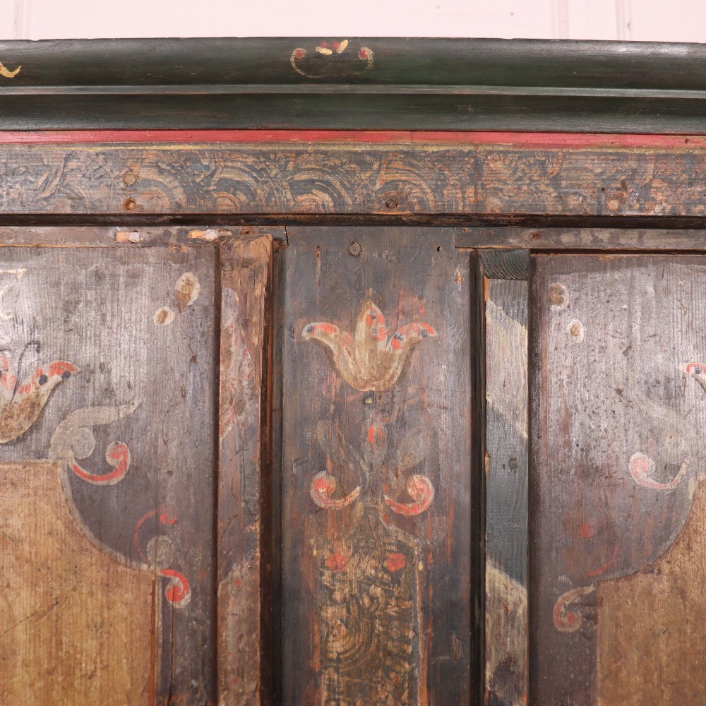 An antique two-door Austrian marriage cupboard featuring hand-painted floral motifs, central ochre panels, a scalloped base apron, and exposed iron strap hinges. View VII