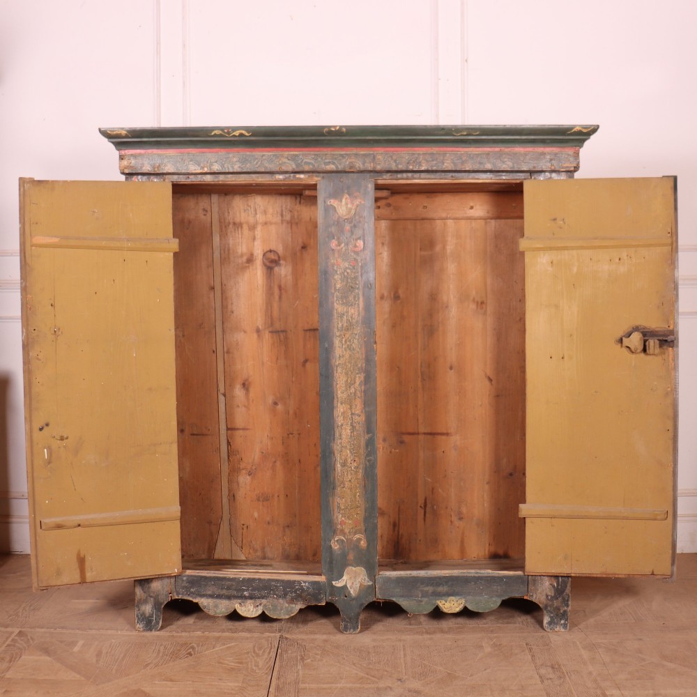 An antique two-door Austrian marriage cupboard featuring hand-painted floral motifs, central ochre panels, a scalloped base apron, and exposed iron strap hinges. View VIII