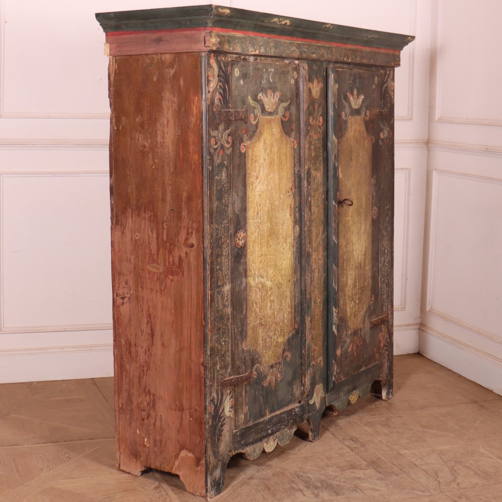 An antique two-door Austrian marriage cupboard featuring hand-painted floral motifs, central ochre panels, a scalloped base apron, and exposed iron strap hinges. View XI