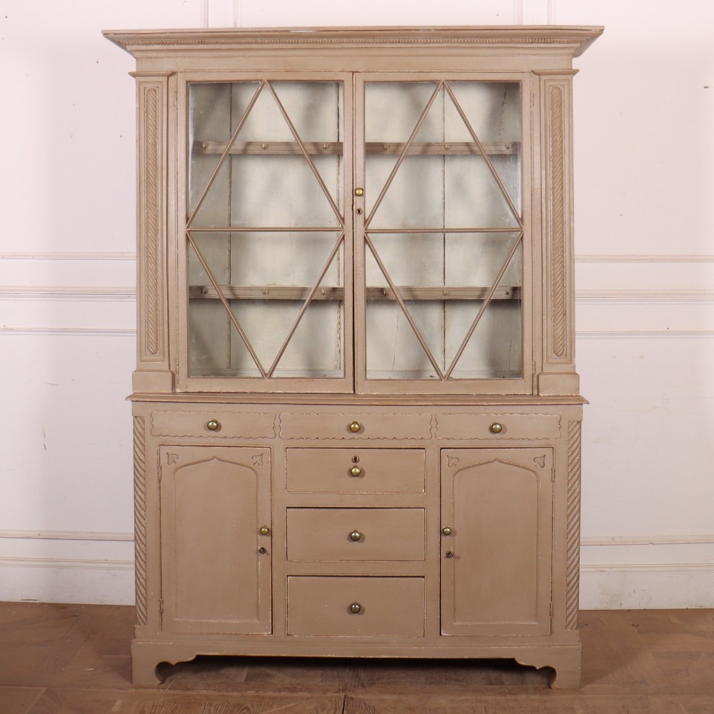 A two-part painted kitchen dresser featuring a glazed upper cabinet with geometric diamond glazing bars over a base with drawers and panelled doors.
