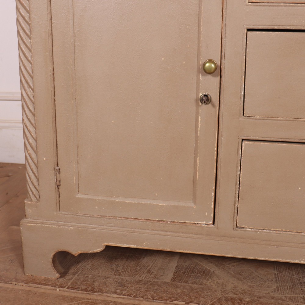 A two-part painted kitchen dresser featuring a glazed upper cabinet with geometric diamond glazing bars over a base with drawers and panelled doors. View VI