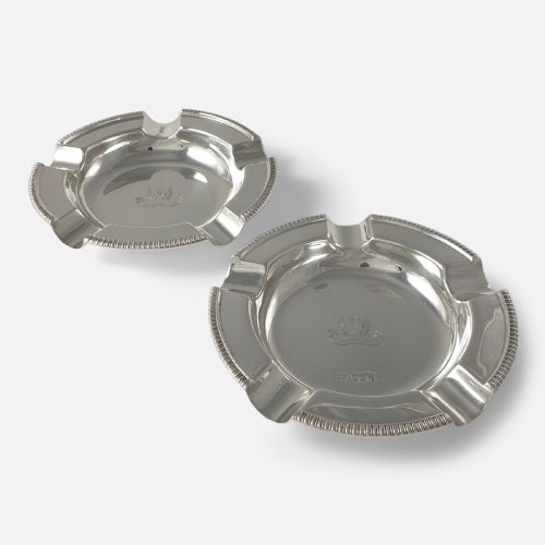 fig 2. A pair of round sterling silver ashtrays featuring engraved central crests, visible hallmarks, and gadrooned rims with cigarette rests.