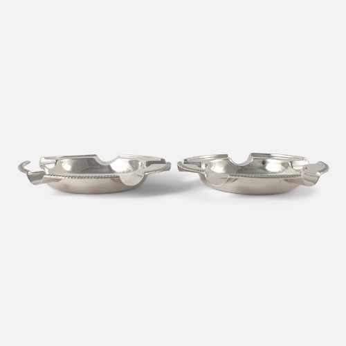 fig 3. A pair of round sterling silver ashtrays featuring engraved central crests, visible hallmarks, and gadrooned rims with cigarette rests.