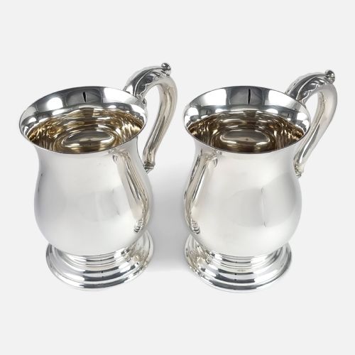 fig 1. A pair of polished sterling silver mugs featuring baluster-shaped bodies, stepped circular pedestal bases, and curved scroll handles.