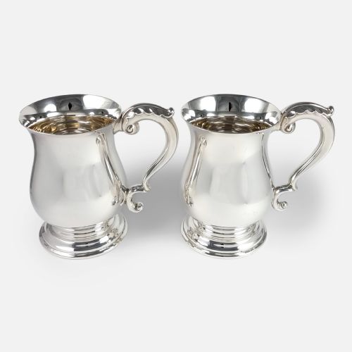 fig 2. A pair of polished sterling silver mugs featuring baluster-shaped bodies, stepped circular pedestal bases, and curved scroll handles.