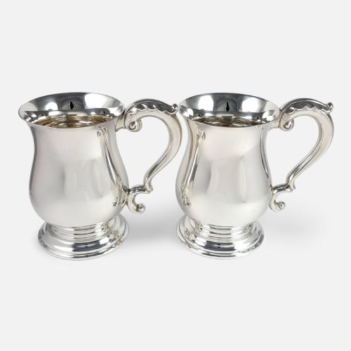 fig 3. A pair of polished sterling silver mugs featuring baluster-shaped bodies, stepped circular pedestal bases, and curved scroll handles.