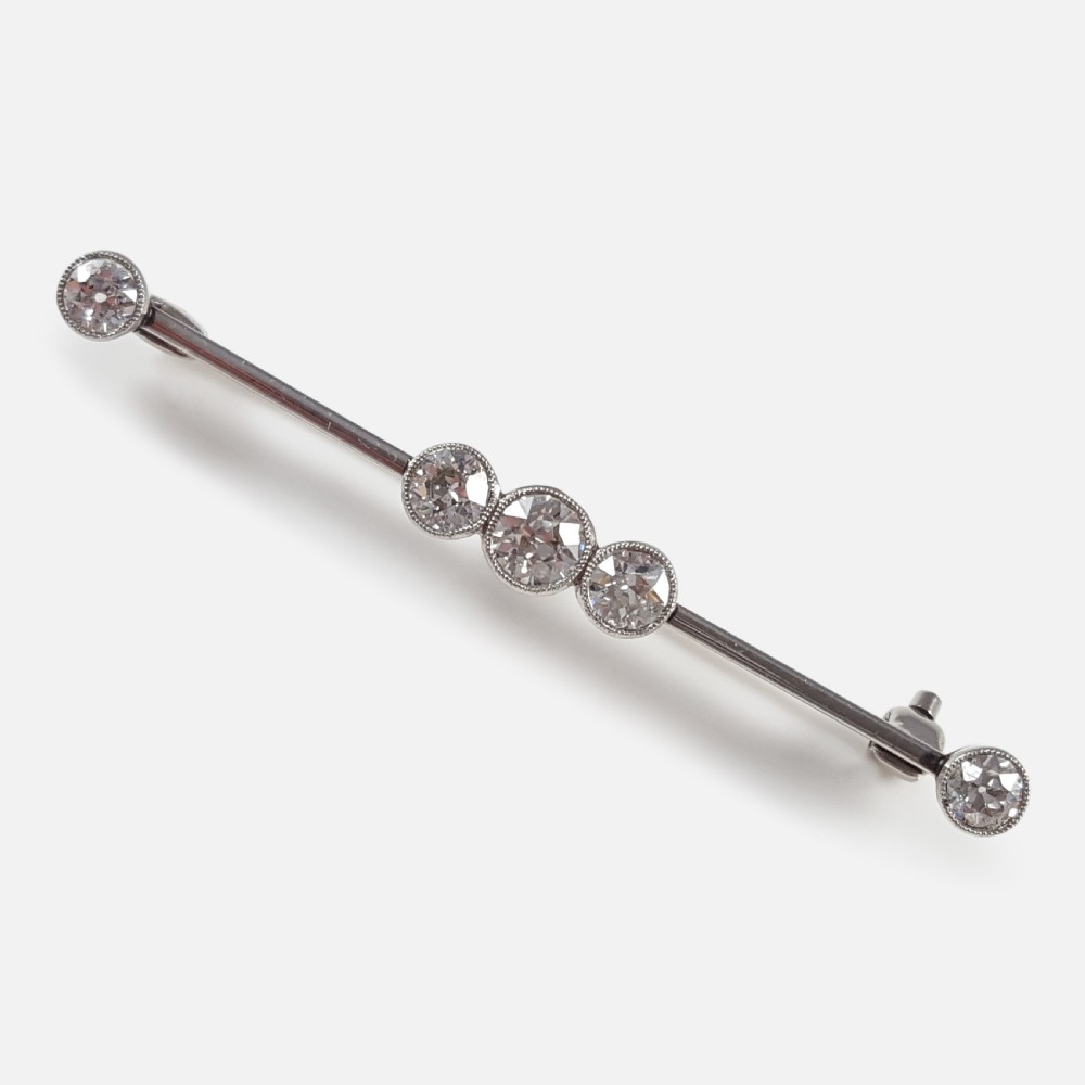 An Art Deco 18ct gold bar brooch set with five round diamonds in millegrain bezel settings.