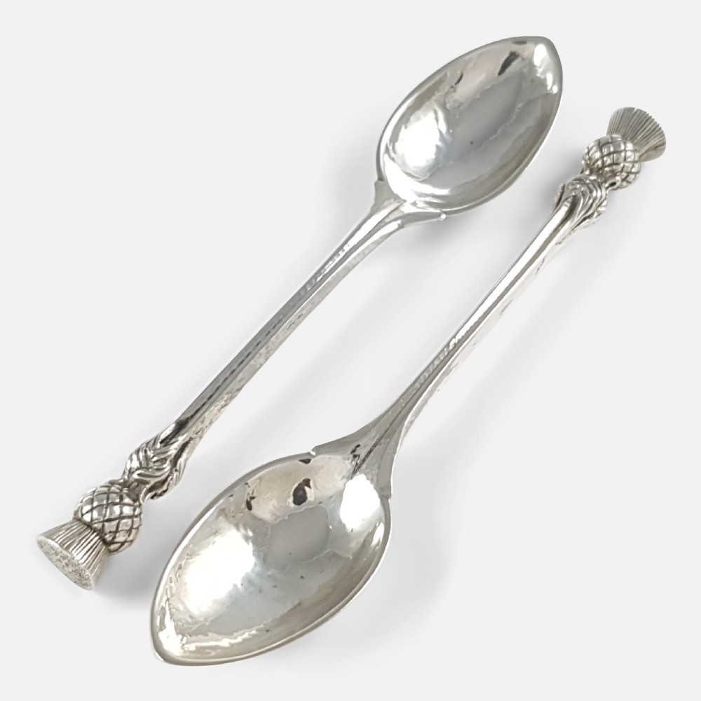 A pair of hand-hammered sterling silver spoons featuring decorative thistle finials and tapered stems.