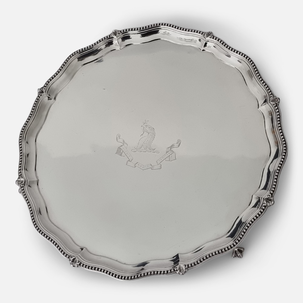 A circular Victorian sterling silver salver with a beaded scalloped rim, small feet, and a central engraved crest.