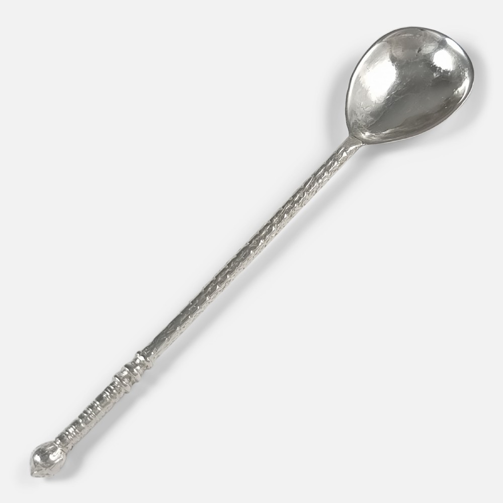 A sterling silver spoon featuring a hand-hammered oval bowl and a long textured stem terminating in a rounded knop finial.