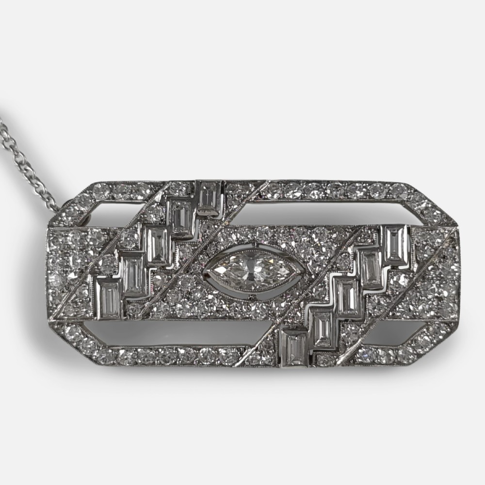 A rectangular Art Deco platinum brooch featuring geometric openwork set with round, baguette, and a central marquise-cut diamond.