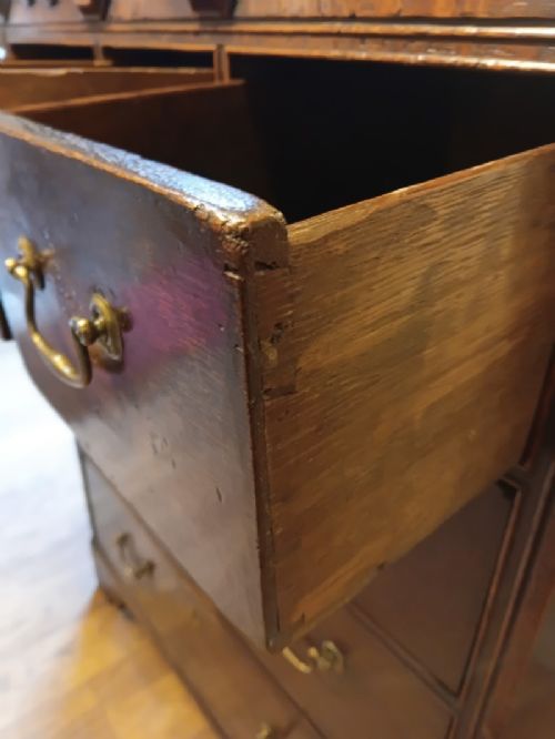 An antique brown oak chest of drawers featuring three small upper drawers over three long graduated drawers with brass drop handles. View VII
