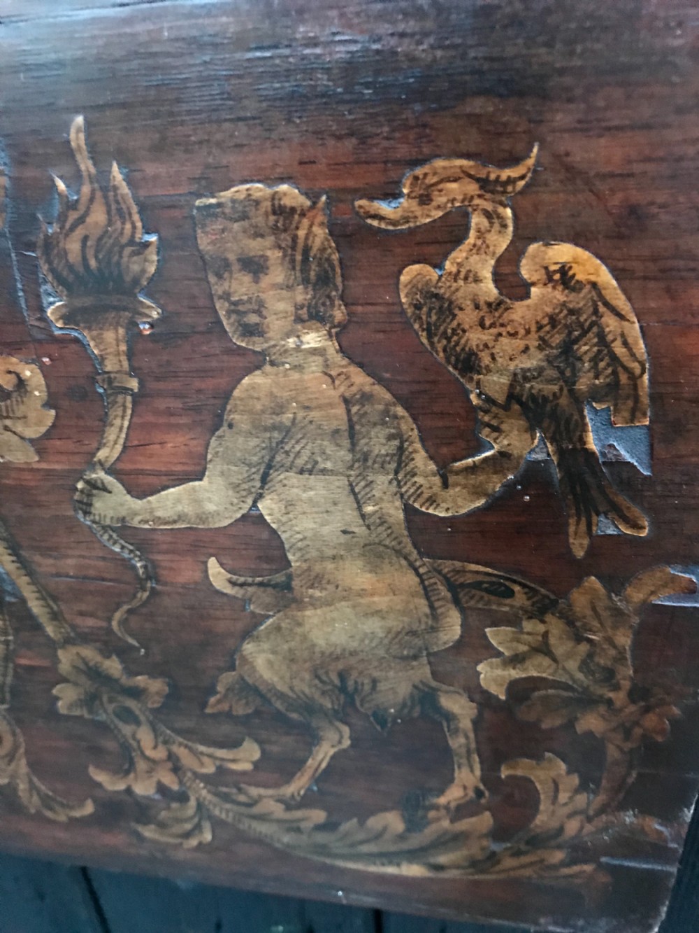 A rectangular antique wooden panel featuring detailed figurative and floral marquetry inlay work in lighter wood tones against a darker wood background. View VI