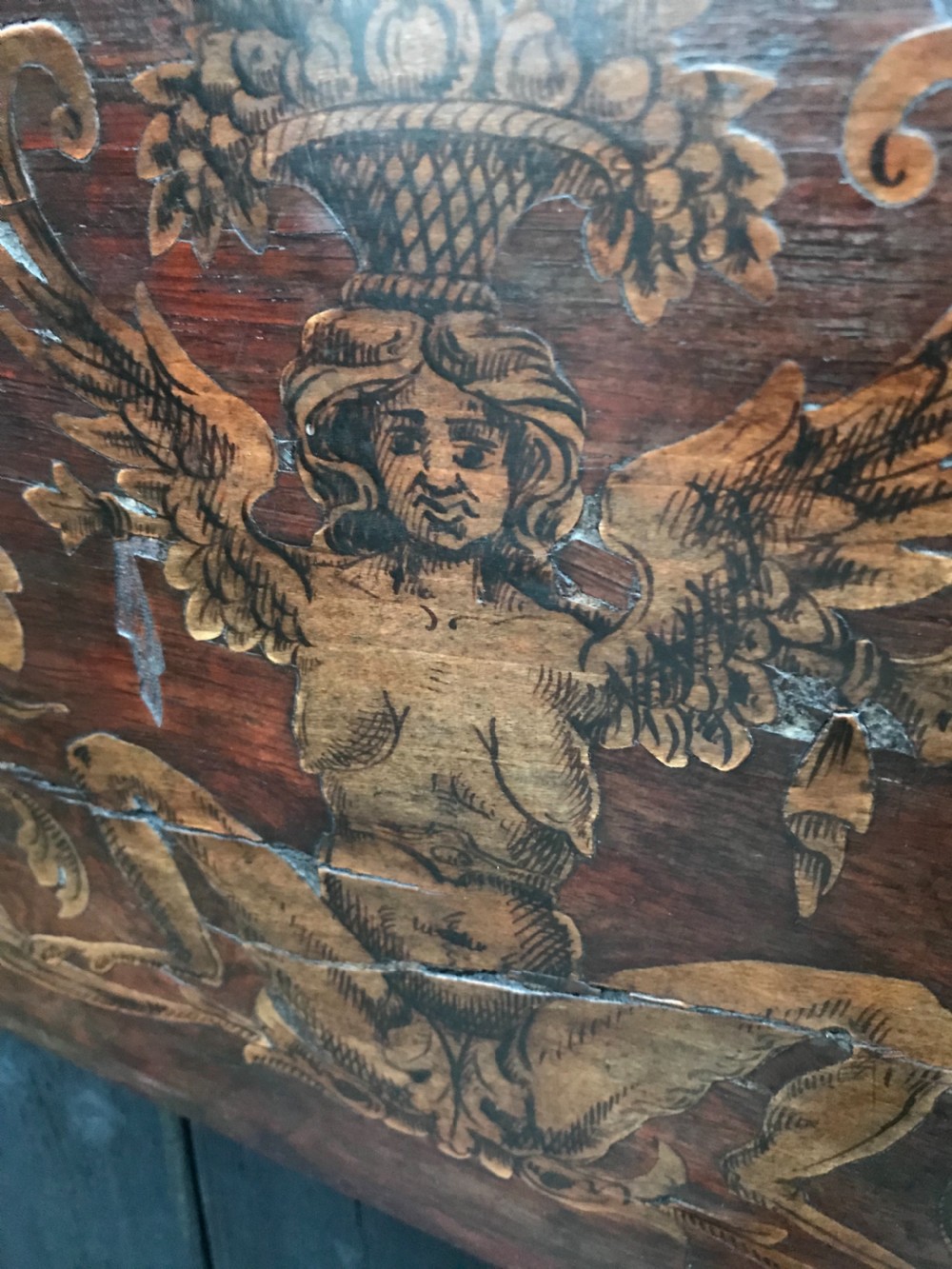 A rectangular antique wooden panel featuring detailed figurative and floral marquetry inlay work in lighter wood tones against a darker wood background. View VII