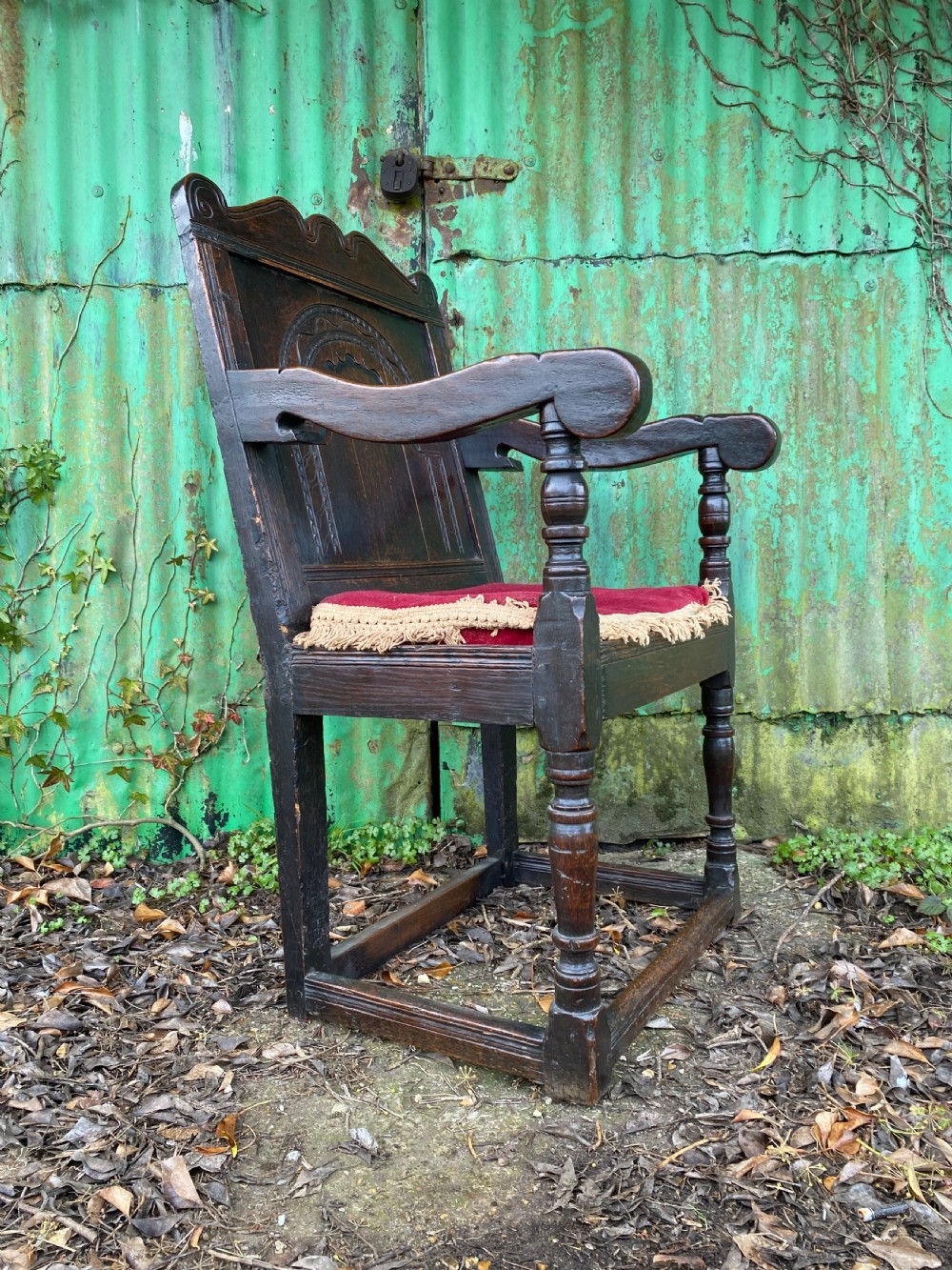 Carved dark oak wainscot armchair featuring an arched back panel, turned front supports, and a red velvet seat cushion with fringe trim. View II
