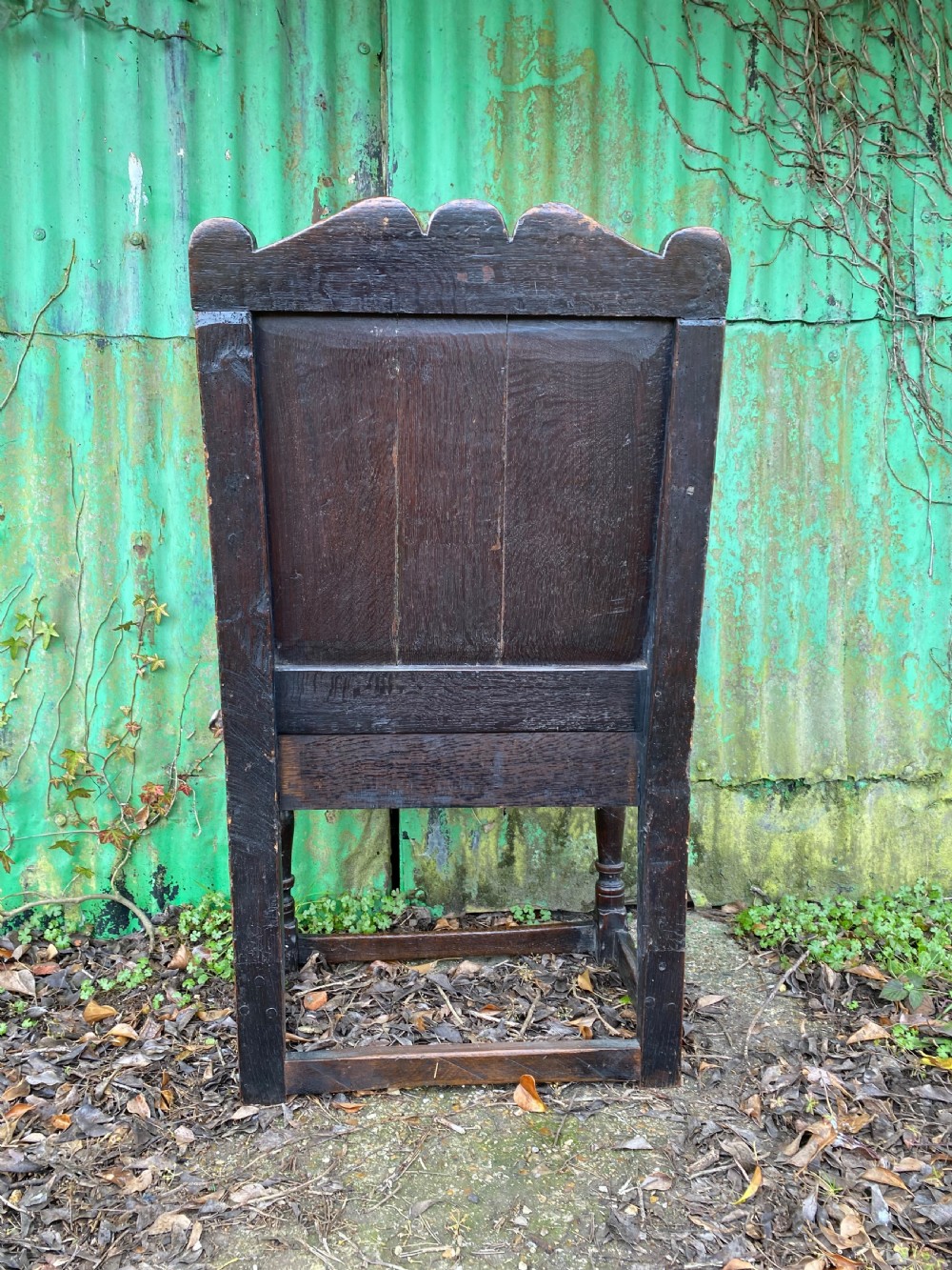 Carved dark oak wainscot armchair featuring an arched back panel, turned front supports, and a red velvet seat cushion with fringe trim. View VI