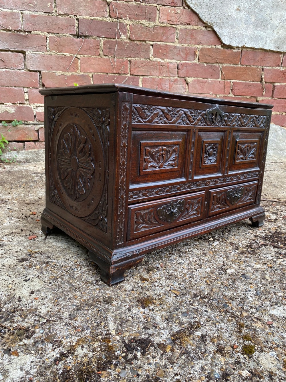 A carved dark oak Georgian coffer bach featuring a hinged lid, relief-carved floral panels, two lower drawers, and bracket feet.