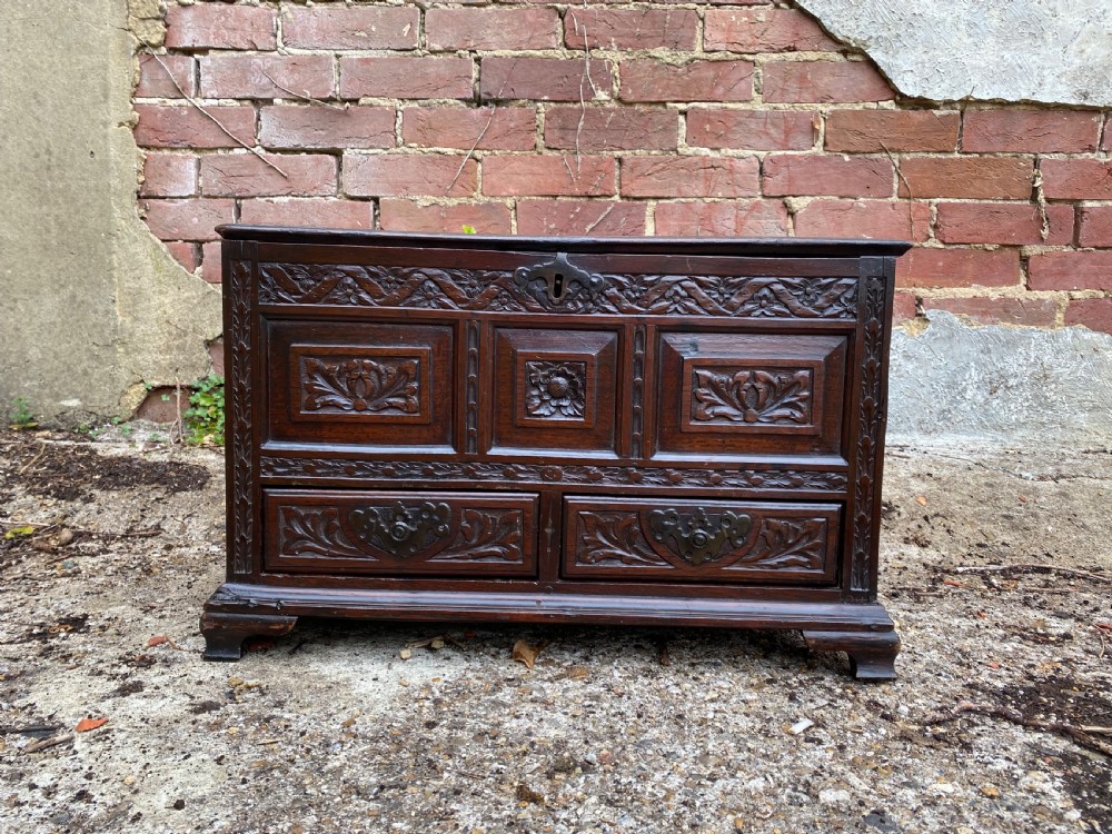 A carved dark oak Georgian coffer bach featuring a hinged lid, relief-carved floral panels, two lower drawers, and bracket feet. View II