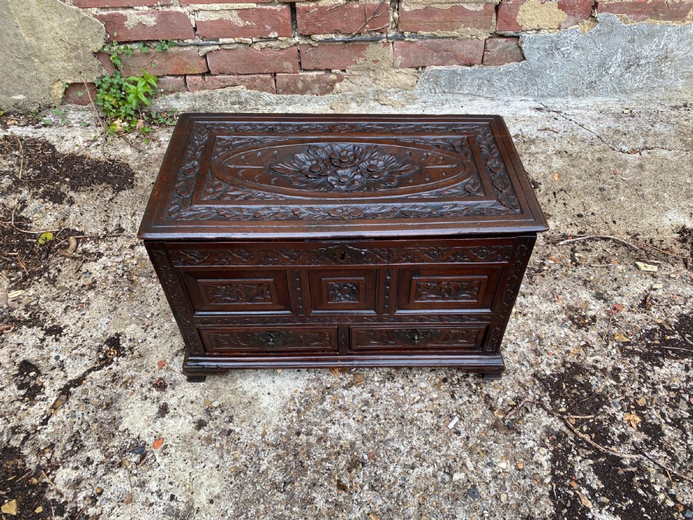 A carved dark oak Georgian coffer bach featuring a hinged lid, relief-carved floral panels, two lower drawers, and bracket feet. View V