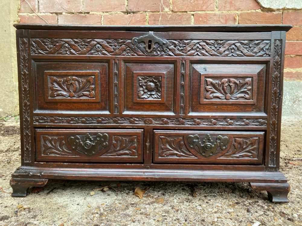 A carved dark oak Georgian coffer bach featuring a hinged lid, relief-carved floral panels, two lower drawers, and bracket feet. View VI