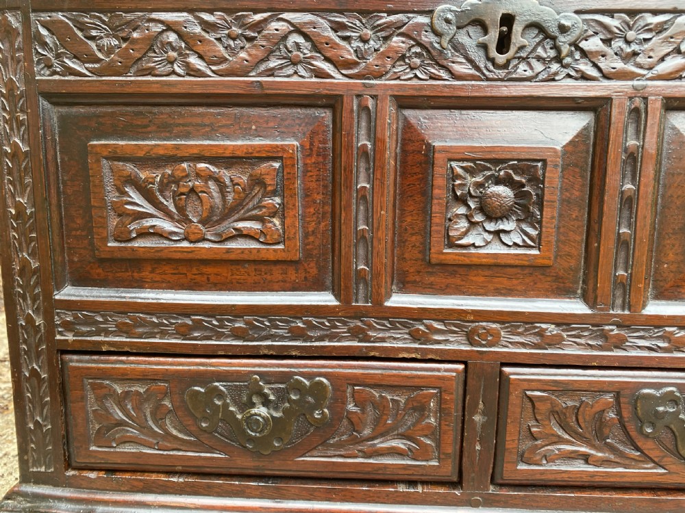 A carved dark oak Georgian coffer bach featuring a hinged lid, relief-carved floral panels, two lower drawers, and bracket feet. View VII