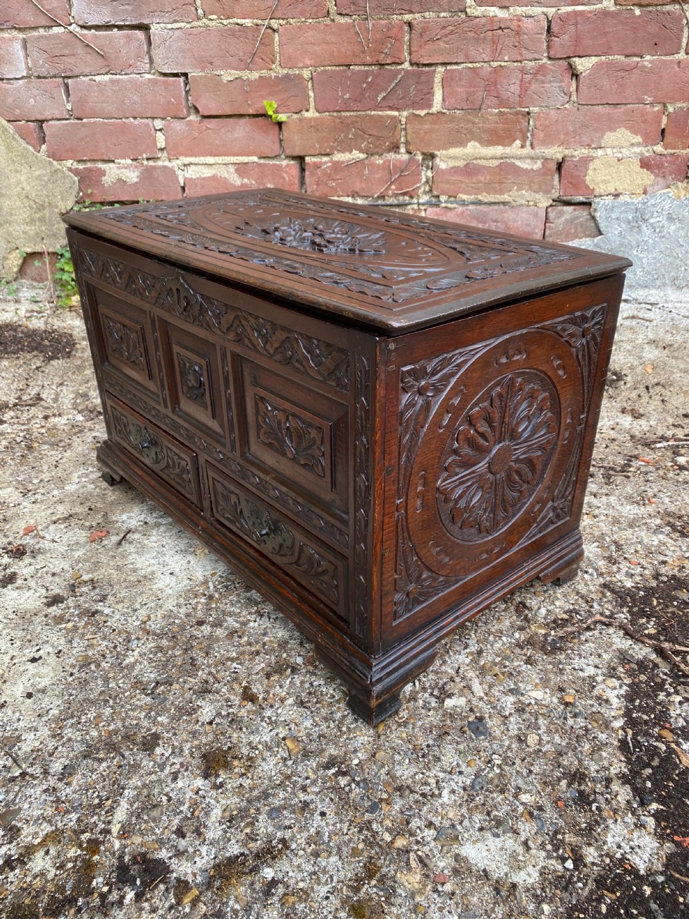 A carved dark oak Georgian coffer bach featuring a hinged lid, relief-carved floral panels, two lower drawers, and bracket feet. View IX